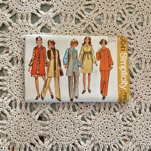 May include: A vintage Simplicity sewing pattern packet featuring illustrations of women's clothing designs. The packet showcases various outfits, including pantsuits and dresses, in a retro style. The packet is rectangular and has the number 9041 printed on it.