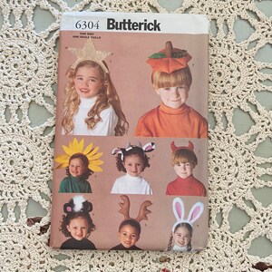 Könnte beinhalten: Ein Vintage-Nähmuster für Kinder-Halloweenkostüme. Das Muster ist für eine Vielzahl von Kostümen, darunter ein Kürbis, eine Sonnenblume, eine Kuh, ein Teufel, ein Waschbär, ein Rentier und ein Kaninchen. Das Muster ist von Butterick und trägt die Nummer 6304. Das Muster ist für eine Größe.
