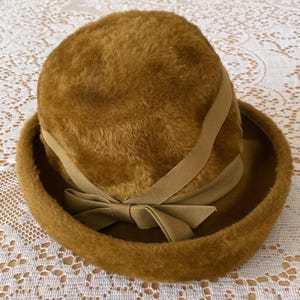 May include: A brown faux fur hat with a wide brim and a brown satin ribbon tied in a bow at the front.