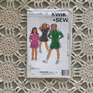 May include: A sewing pattern for girls' dresses, sizes 8-10-12-14. The pattern shows three different styles of dresses: a floral print dress with short sleeves, a pink dress with short sleeves and a green dress with long sleeves. The pattern is from Kwik Sew Pattern Co. Inc.