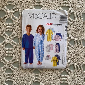 Könnte beinhalten: Ein Schnittmuster für Kinderpyjamas. Das Muster umfasst sechs verschiedene Stile, darunter ein langärmliger Pyjama-Set, ein kurzärmeliger Pyjama-Set, ein Morgenmantel und ein Pyjama mit Kapuze. Das Muster ist für die Größen 1-2-3. Das Muster ist von McCall's und heißt "Easy Endless Options".