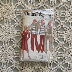 Könnte beinhalten: Ein Vintage-Schnittmuster von Butterick, Größe 12, mit Illustrationen von Damenbekleidung. Das Schnittmusterpaket zeigt Abbildungen eines Kleides, einer Jacke und einer Hose. Der Hintergrund ist eine cremefarbene Häkeldecke.