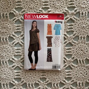 Op de afbeelding: Een naaipatroon voor vier verschillende tops. Het patroon is van New Look en is gemarkeerd met "easy". De tops zijn allemaal in verschillende stijlen en kleuren, waaronder een bruine top met een ruche, een blauwe top met een ruche, een bloementop met een ruche en een zwart-witte top met een ruche.