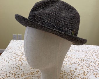 Könnte beinhalten: Ein grauer Tweed-Fedora-Hut mit leicht gebogenem Rand. Der Hut sitzt auf einem weißen Mannequin-Kopf.