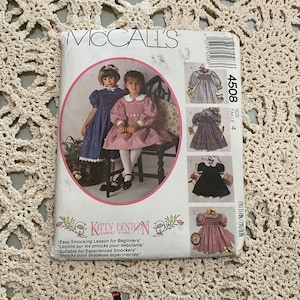 May include: A vintage McCall's sewing pattern for a smocked dress for girls. The pattern is for sizes 4, and the pattern number is 4508. The pattern is titled "Kitty Benton Gourmet Sewing" and includes instructions for "Easy Smocking Lesson for Beginners", "Leçons sur les smocks pour débutante", "Suitable for Experienced Smockers", and "Smocks pour brodeuse expérimentée".