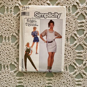 Könnte beinhalten: Simplicity Schnittmuster Nummer 8495 für ein Kleid und eine Latzhose. Das Schnittmuster ist für die Größen PT und zeigt ein Model, das ein gestreiftes Kleid mit Gürtel trägt, und ein Model, das eine Latzhose trägt.