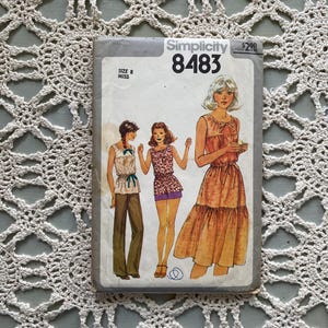 May include: A vintage Simplicity 8483 sewing pattern with illustrations of three outfits. The pattern is for a size 8 Miss. The cover art shows a woman in a dress, a top and trousers, and a top and shorts.