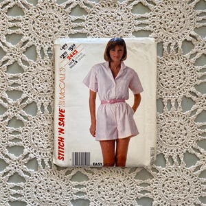 May include: A sewing pattern for a short-sleeved, collared jumpsuit with a pink and white striped pattern. The pattern is from McCall's and is called "Stitch 'n Save". The pattern number is 2443 and the size is B (12-14-16).