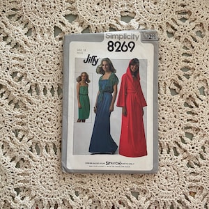 Könnte beinhalten: Simplicity Schnittmuster Nummer 8269 für ein Jiffy-Kleid, das nur für dehnbare Strickwaren geeignet ist. Das Schnittmuster enthält drei verschiedene Kleidmodelle: ein grünes ärmelloses Kleid, ein blaues Kleid mit kurzen Ärmeln und ein rotes Kleid mit Kapuze.