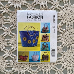 May include: A McCall's Fashion Accessories sewing pattern packet featuring images of various handbags. The main image shows a blue tote bag with yellow sunflowers and wooden handles. The packet is labeled M4885.