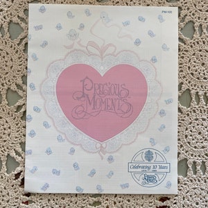 May include: A white card with a pink heart in the center. The heart has the words "Precious Moments" written in cursive. The card is surrounded by small blue birds. The card has the text "Celebrating 10 Years 1979 - 1989" and a logo that says "Precious Moments".