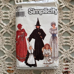May include: A vintage Simplicity sewing pattern packet featuring illustrations of various costume designs. The packet includes images of a witch, angel, and other historical or fantasy-themed outfits. The packet is white with black text and illustrations.