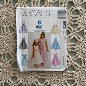 May include: A McCall's sewing pattern featuring eight dress designs. The pattern packet shows illustrations of various dresses, including floral, solid, and patterned styles. The text on the packet reads "Great Looks One Easy Pattern".