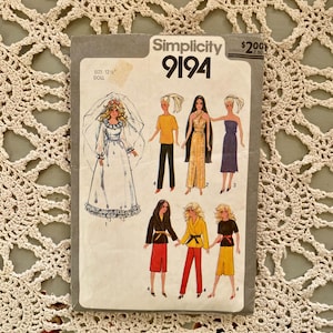 Puede incluir: Patrón de costura Simplicity vintage 9194 para una muñeca de 31,75 cm. El patrón presenta ilustraciones de varios conjuntos de muñecas, incluyendo un vestido de novia, un mono y vestidos. El sobre del patrón es gris con el logotipo de Simplicity y el número de patrón.