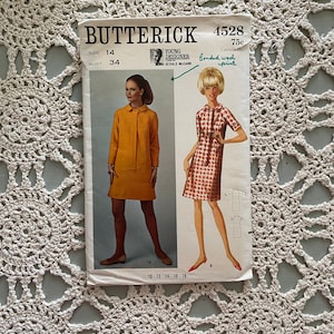 May include: Vintage sewing pattern for a dress, Butterick 4528, size 14, bust 34, designed by Gerald McCann. The pattern is for a dress made with bonded wool print fabric. The pattern includes two different styles of dresses, one with a collar and one without.