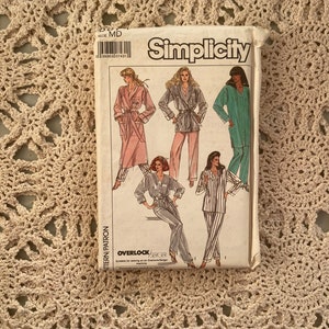 Peut inclure: Un paquet de patrons de couture Simplicity avec des illustrations de pyjamas et de robes pour femmes. Le paquet est blanc avec le nom de la marque "Simplicity". La taille est MD.