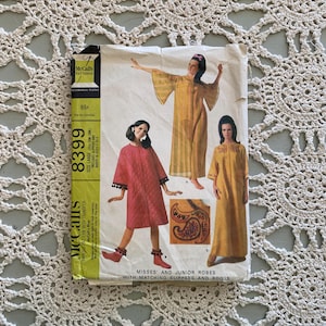 Könnte beinhalten: Vintage McCall's Schnittmuster für Damen- und Junior-Roben mit passenden Hausschuhen und Stiefeln. Das Muster zeigt Illustrationen der Roben in verschiedenen Stilen und Farben, darunter eine rosa Robe mit schwarzem Besatz und eine gelbe Robe. Das Muster ist mit dem Preis von 65¢ gekennzeichnet.
