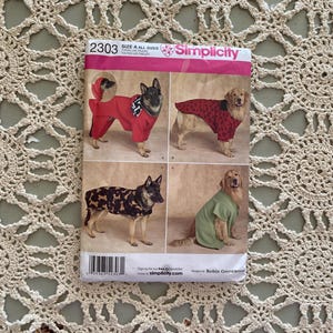 Può includere: Modello di cucito Simplicity numero 2303 per abiti per cani. Il modello include quattro diversi stili di abbigliamento per cani: una tuta rossa con cappuccio, una camicia a pois rossi e neri, una giacca mimetica marrone e nera e una camicia verde. Il modello è stato progettato da Robin Greenwood.