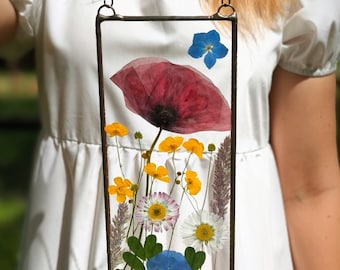 May include: A framed pressed flower art piece with a red poppy, yellow wildflowers, and blue forget-me-nots.