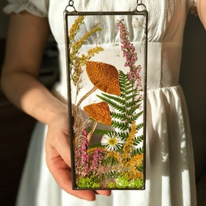 May include: A framed pressed flower art piece featuring dried mushrooms, ferns, and wildflowers in shades of brown, green, pink, and yellow.