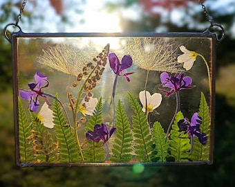 May include: A framed pressed flower art piece with a variety of purple and white flowers, including ferns, pressed between two pieces of glass. The frame is made of metal and has a rustic look.