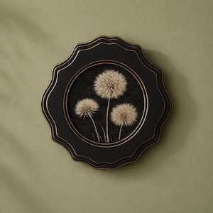 May include: A round, black framed wall art piece featuring three dandelion seed heads against a dark background. The frame has a scalloped edge with gold trim. The artwork is displayed against a muted green backdrop.