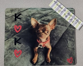 Op de afbeelding: Een bruine en witte chihuahua met grote oren en een rode halsband zit op een grijs, getextureerd oppervlak. De afbeelding heeft de letters "K" en harten erop getekend.
