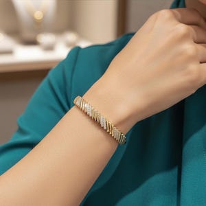 May include: Gold-coloured bracelet with a zig-zag design, embellished with small, sparkling stones. The bracelet is worn on a wrist, highlighting its intricate details and elegant style. A piece of jewellery.
