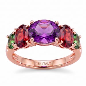 May include: A rose gold ring featuring a large round purple amethyst center stone flanked by two oval red garnet stones and two smaller green peridot stones. The inner band is clearly engraved with the text 18K ITALY, indicating the metal purity.