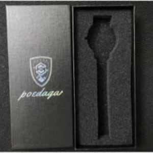 May include: A black rectangular watch box with a textured finish. The lid features a silver shield logo with the text poedaga below it. The interior contains a black foam insert with a cutout shaped to hold a wristwatch securely in place.
