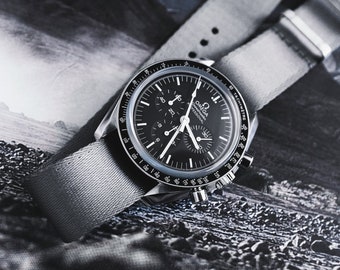 May include: A black and silver wristwatch with a gray fabric band. The watch face has multiple dials and white hands. The watch is set against a black and white landscape background.