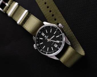 May include: A wristwatch with a black face and silver casing, featuring white hour markers and hands. The watch has a date display and is set on an olive green nylon strap with white stripes. The watch is displayed on a black surface.