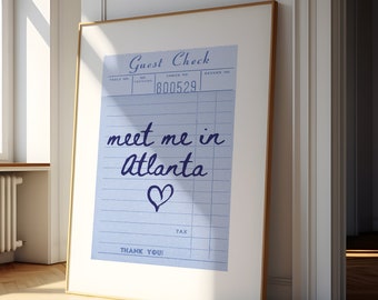 May include: A framed print of a blue and white guest check with the text "meet me in Atlanta" written in purple cursive with a heart drawn below the text. The check number is 1800529.