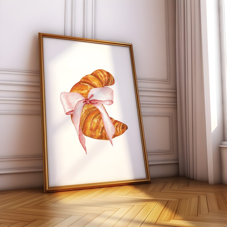 May include: A watercolor illustration of a croissant tied with a pink ribbon. The croissant is a light brown color and the ribbon is a pale pink. The illustration is on a white background.