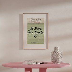 May include: A framed print of a vintage-style guest check with the text "Il Dolce Far Niente" and a heart symbol. The check has a green background and black text. The frame is brown wood.