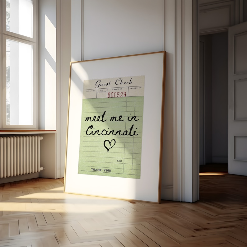 May include: A framed print with a green and white guest check design. The text "meet me in Cincinnati" is written in black cursive with a heart symbol below. The check number is 800529.