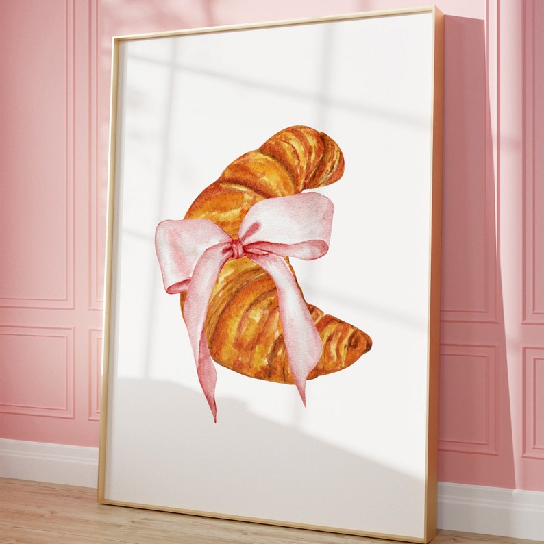 May include: A watercolor painting of a croissant with a pink ribbon tied around it. The croissant is a light brown color and the ribbon is a pale pink with a darker pink bow.