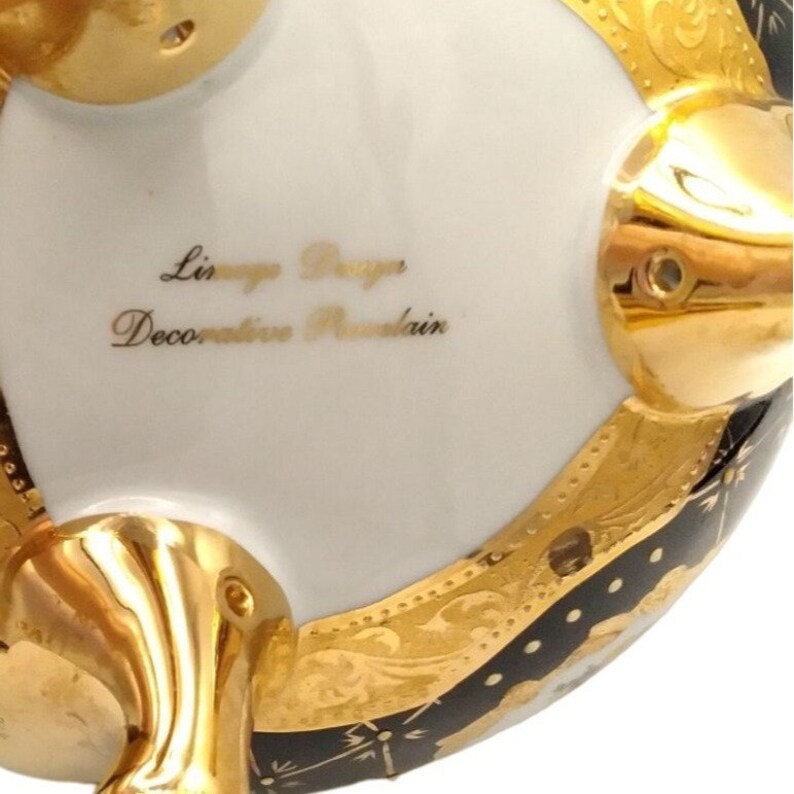 May include: A white porcelain decorative mountain with gold accents and black detailing. The bottom of the mountain has three gold feet. The mountain has the text "Limoges Design Decorative Mountain" written on the bottom.