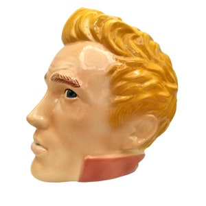 Könnte beinhalten: Eine Keramiktasse in Form eines Männerkopfes mit blonden Haaren. Die Tasse hat einen rosa Kragen und blaue Augen.