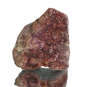 Può includere: Una roccia ruvida di forma irregolare con un gruppo di piccoli cristalli rosa. I cristalli sono densamente impacchettati e conferiscono alla roccia un aspetto scintillante.