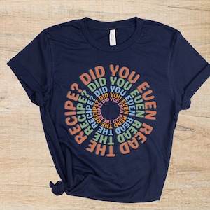 May include: A navy blue t-shirt with a circular design featuring the text "Did you even read the recipe?" in a rainbow of colors.