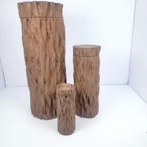 May include: Three wooden containers shaped like tree trunks. The largest container is about 10 inches tall, the middle container is about 6 inches tall, and the smallest container is about 4 inches tall.