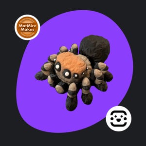 May include: A handmade spider ornament with an orange and tan body, black and white striped legs, and large white eyes. The spider has a black abdomen. The background is a purple circle on a dark grey background. The text "MatMire Makes" is visible.