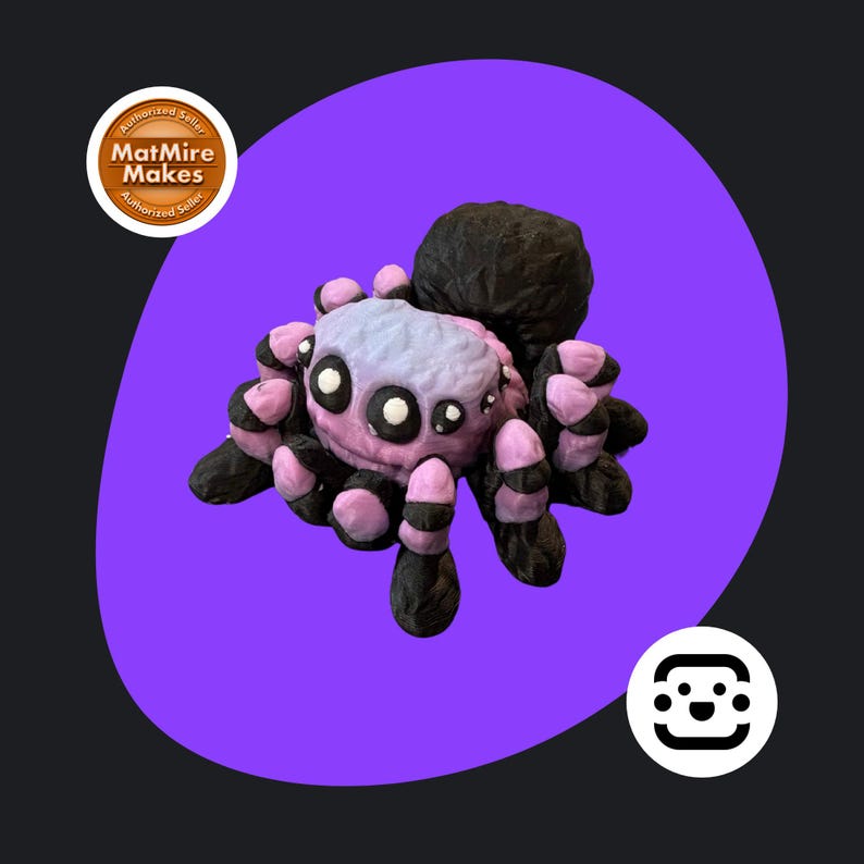 May include: A handmade spider ornament with a black body and legs, and a pink and lilac head. The spider has white eyes and is set against a purple backdrop. The figurine is a unique decorative item.
