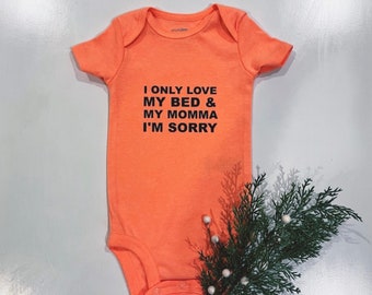 May include: A bright orange baby onesie with black text that reads "I only love my bed & my momma I'm sorry".