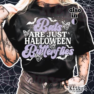 May include: Black t-shirt with the text "Bats Are Just Halloween Butterflies" in white and lavender. The design includes bats and butterfly graphics. A Halloween-themed graphic tee.