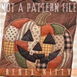 May include: A brown t-shirt featuring a large, quilted-style pumpkin graphic with a jack-o'-lantern face. The pumpkin is composed of various fabric patches in orange, green, and beige with floral, plaid, and polka dot patterns. Text reads NOT A PATTERN FILE and REBEL KITTY.