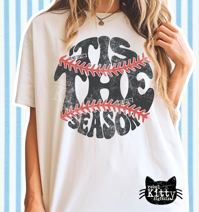 May include: Cream-colored t-shirt with a distressed baseball graphic. The graphic reads "'TIS THE SEASON" in a retro font, with a baseball design in the center. The shirt has a relaxed fit and a small black cat logo at the bottom.