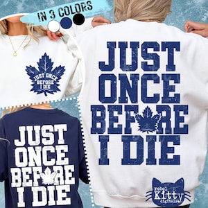 Op de afbeelding: Witte, marineblauwe en zwarte sweatshirts met de tekst "JUST ONCE BEFORE I DIE" en een esdoornblad-afbeelding. De voorkant van een sweatshirt heeft de tekst en de afbeelding, terwijl de achterkant van een ander dezelfde tekst heeft. De afbeelding toont de sweatshirts in drie kleuren.