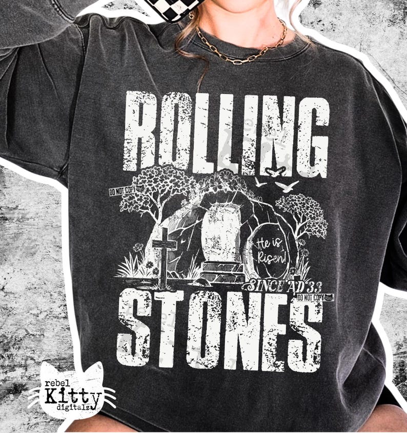 May include: Dark gray sweatshirt with the words "ROLLING STONES" in a distressed white font. The graphic includes a cross, tomb, trees, and the text "He is Risen! Since AD 33". The sweatshirt has a vintage, worn look.